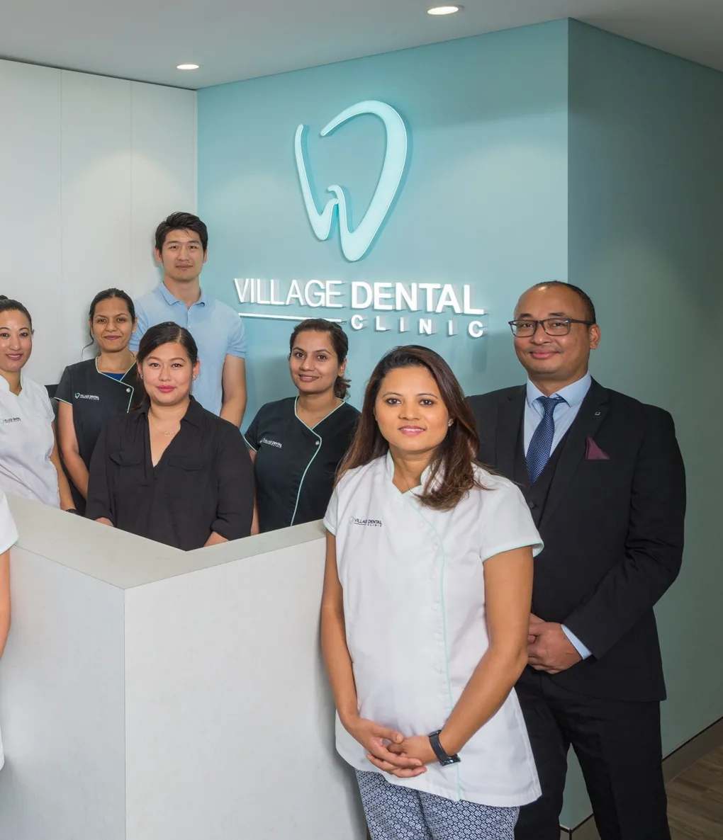 The Village Dental Clinic team at the reception desk beneath the practice's backlit logo